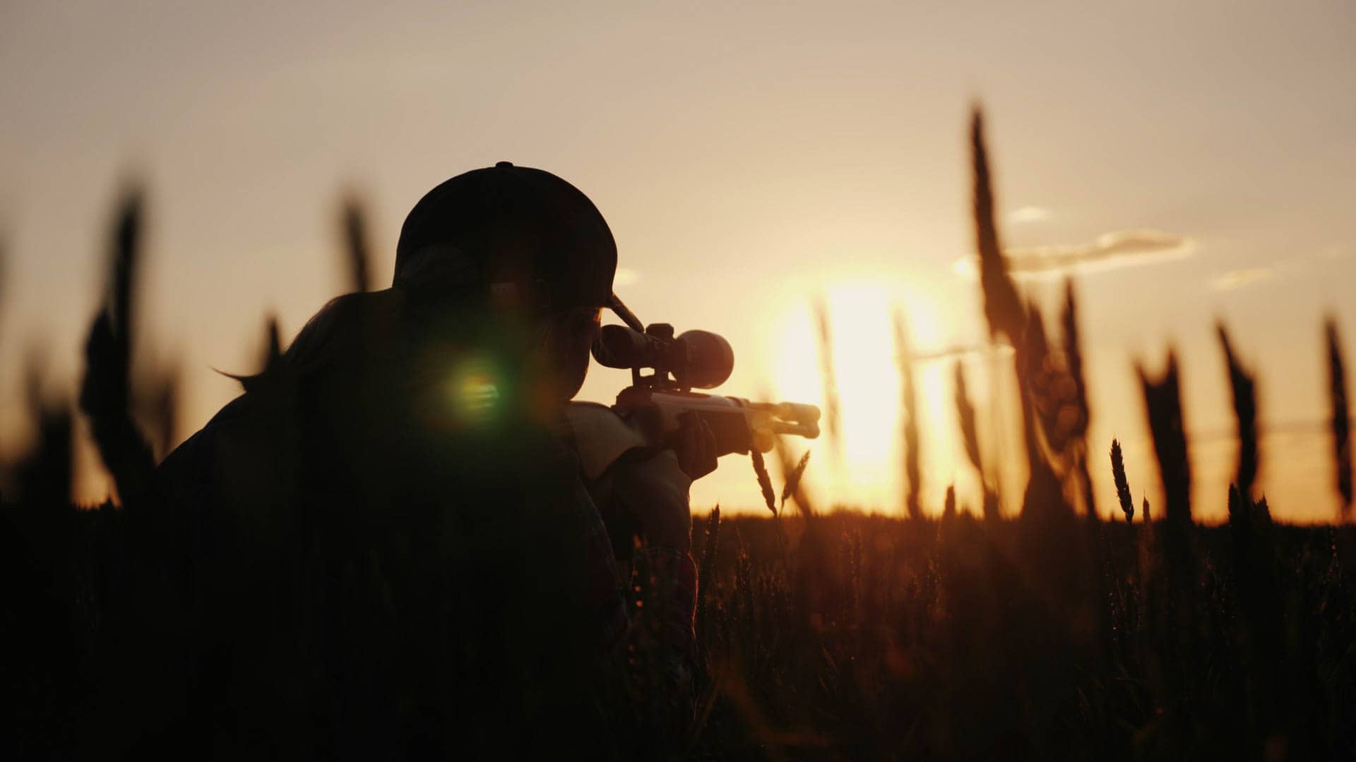 Silhouette aiming rifle at sunset in field