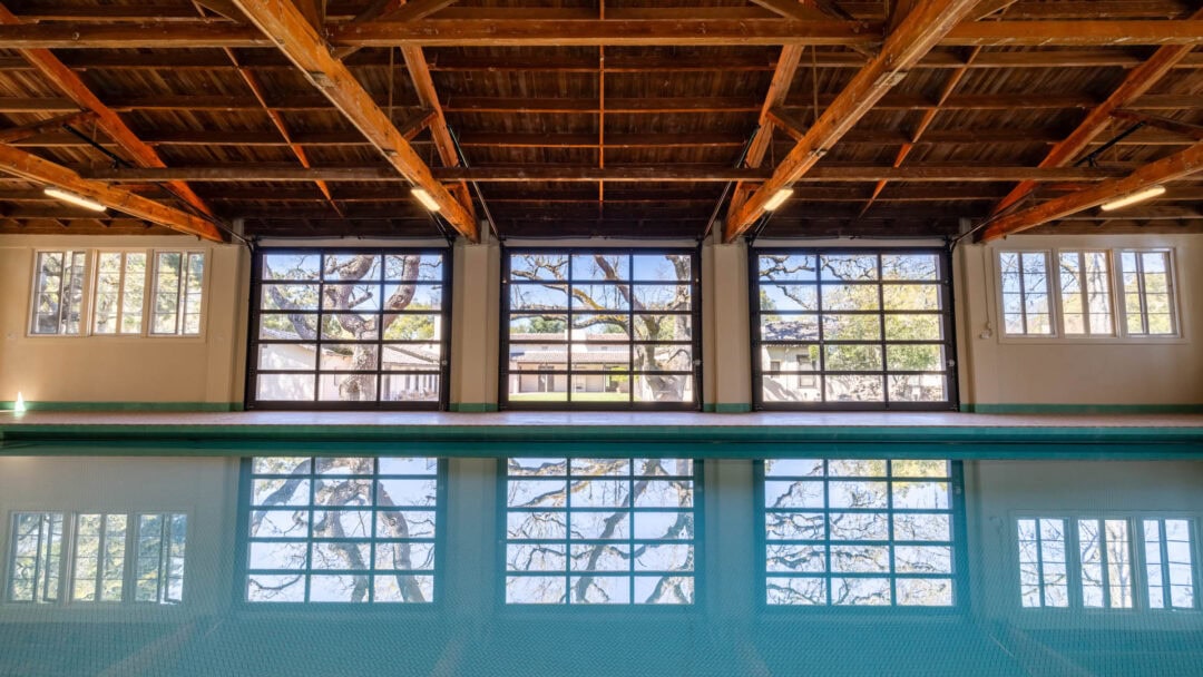 Indoor pool with large windows and wooden ceiling.