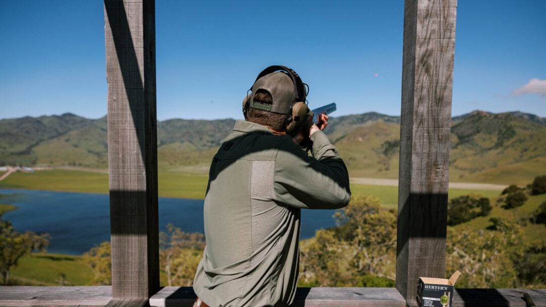 Person shooting in outdoor range with scenic background.