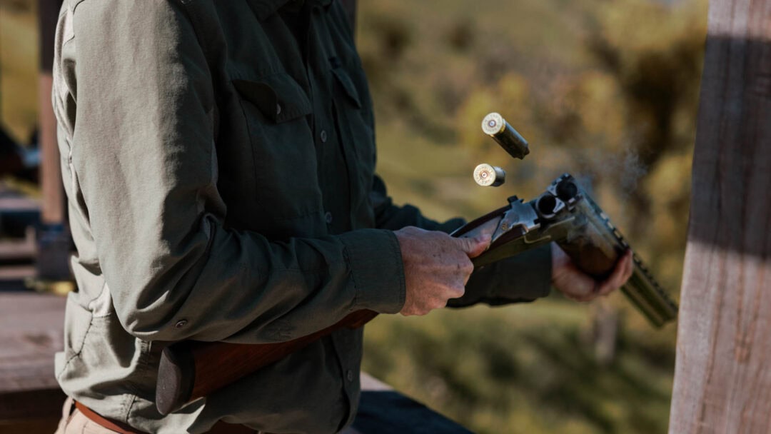 Person reloading a double-barrel shotgun outdoors.