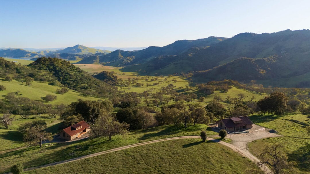 Scenic valley with two houses, hills in background.