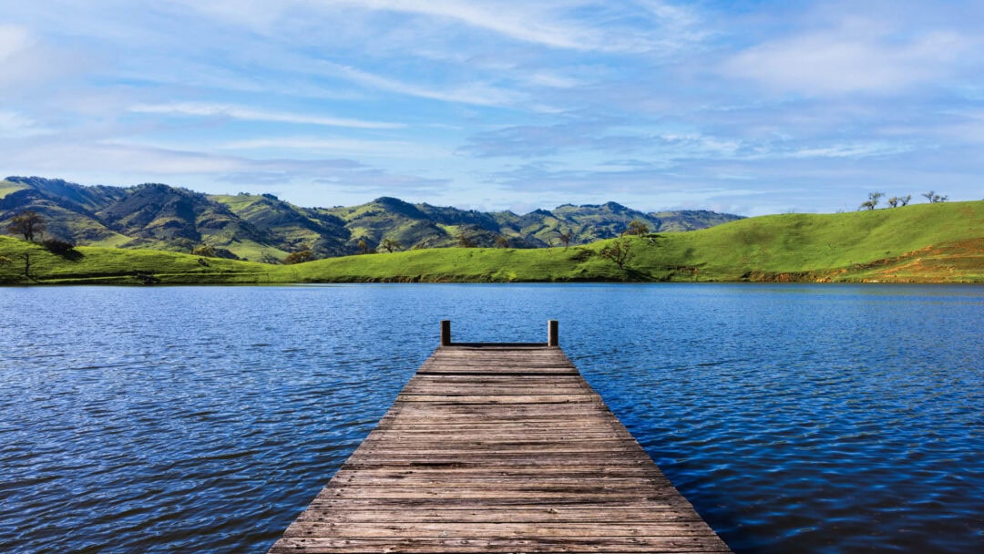 Lake with mountain view and wooden dock.